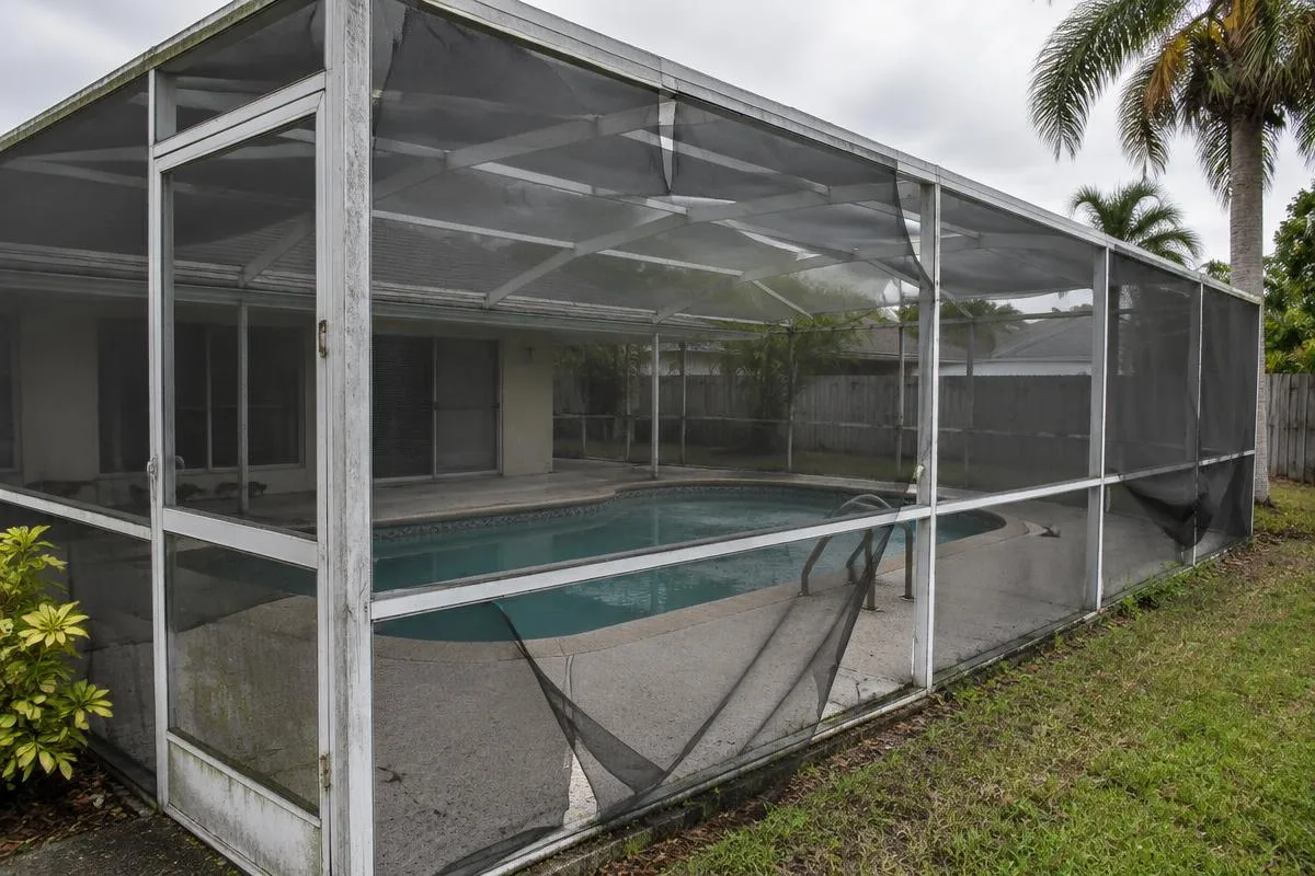 Older white aluminum pool enclosure with faded frame and torn screen panels